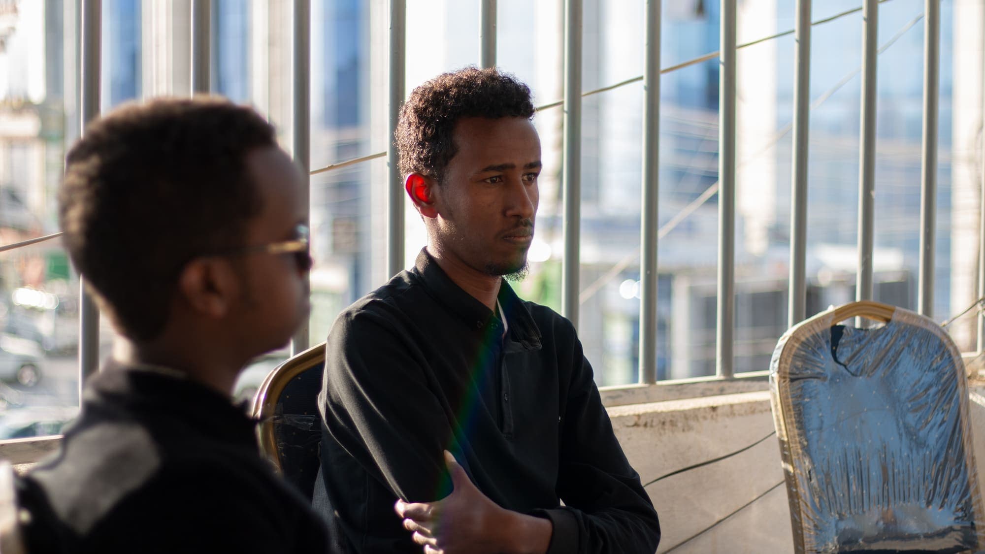 Two men seated by a window talk to each other