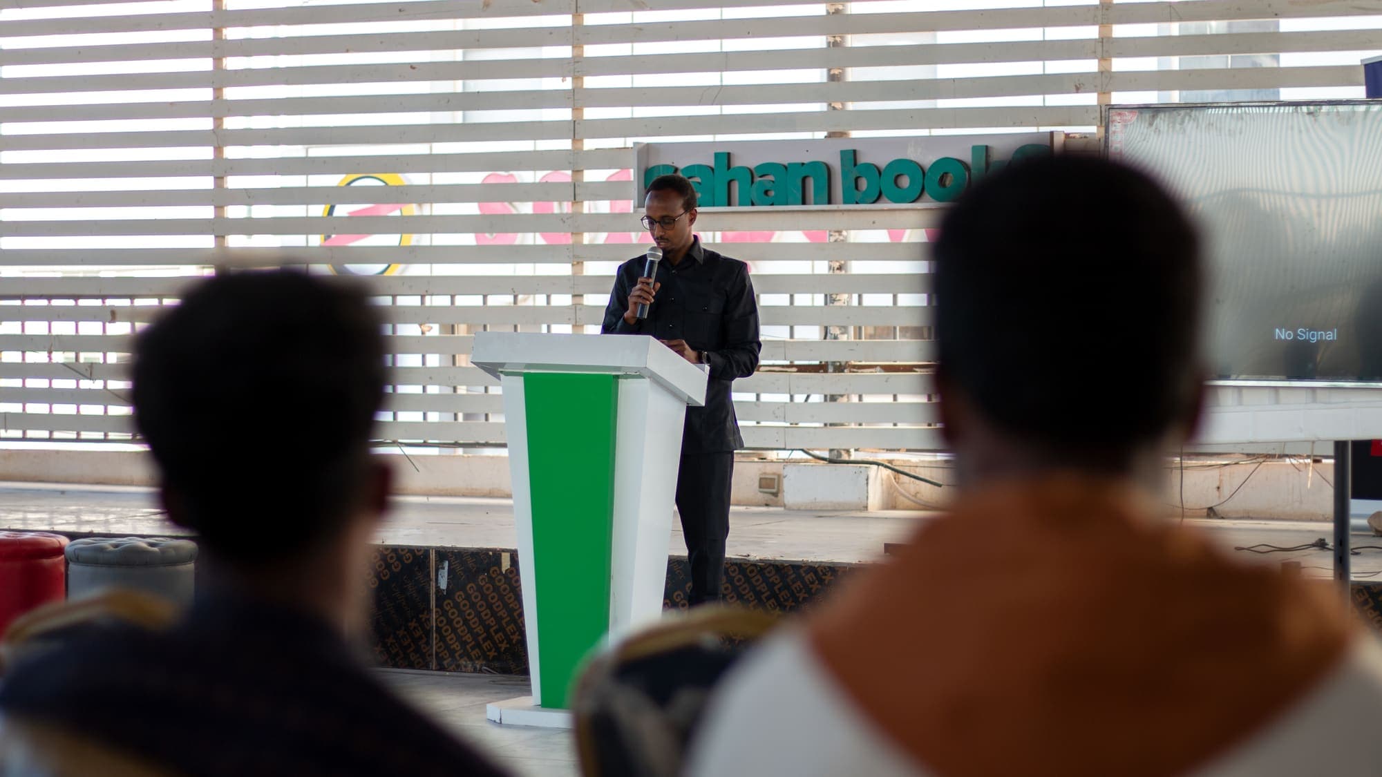 A speaker at the podium addresses a seated audience